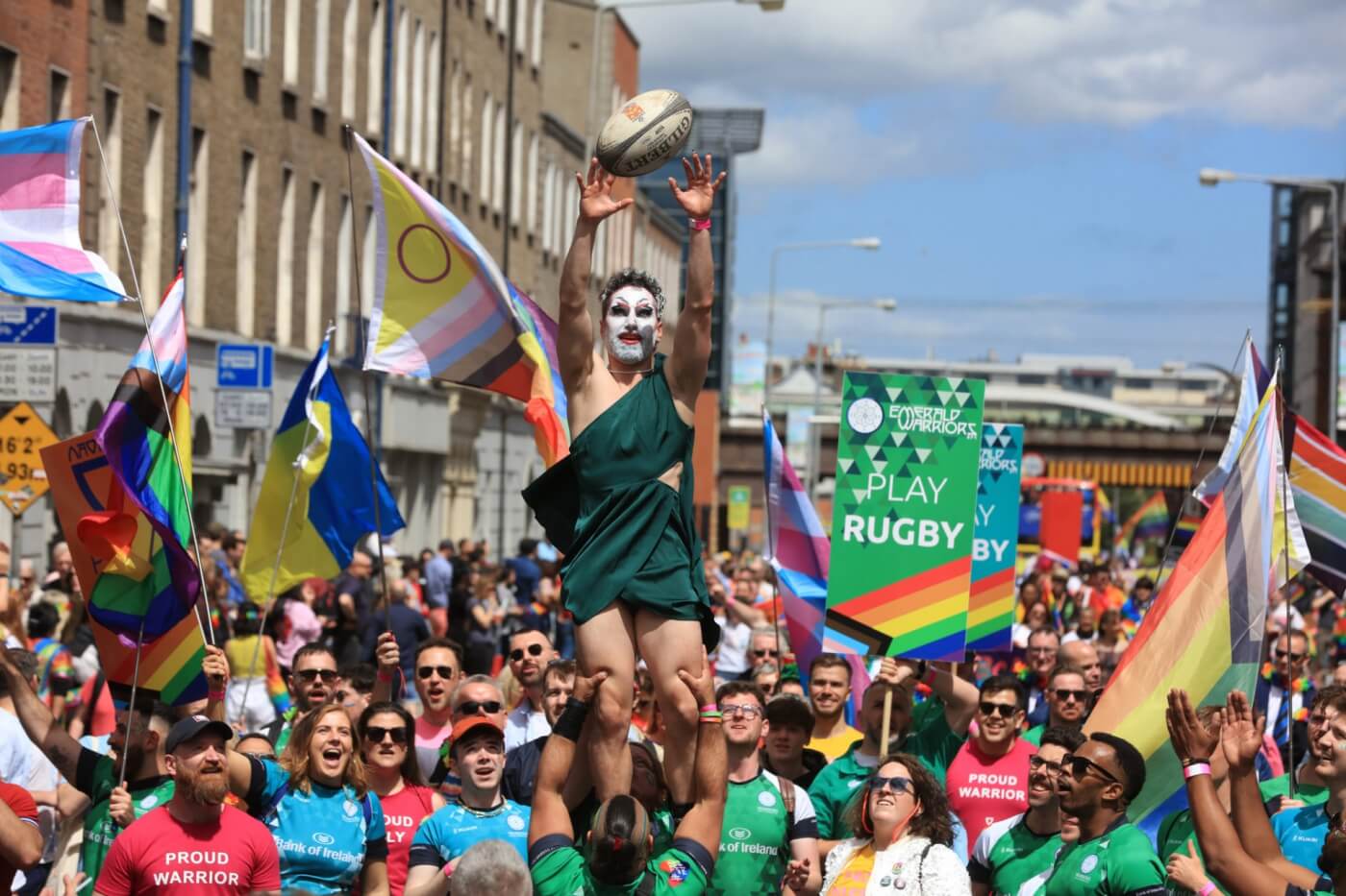 Celebración del Pride en Dublín en verano con banderas arcoíris y un jugador de rugby en el aire.