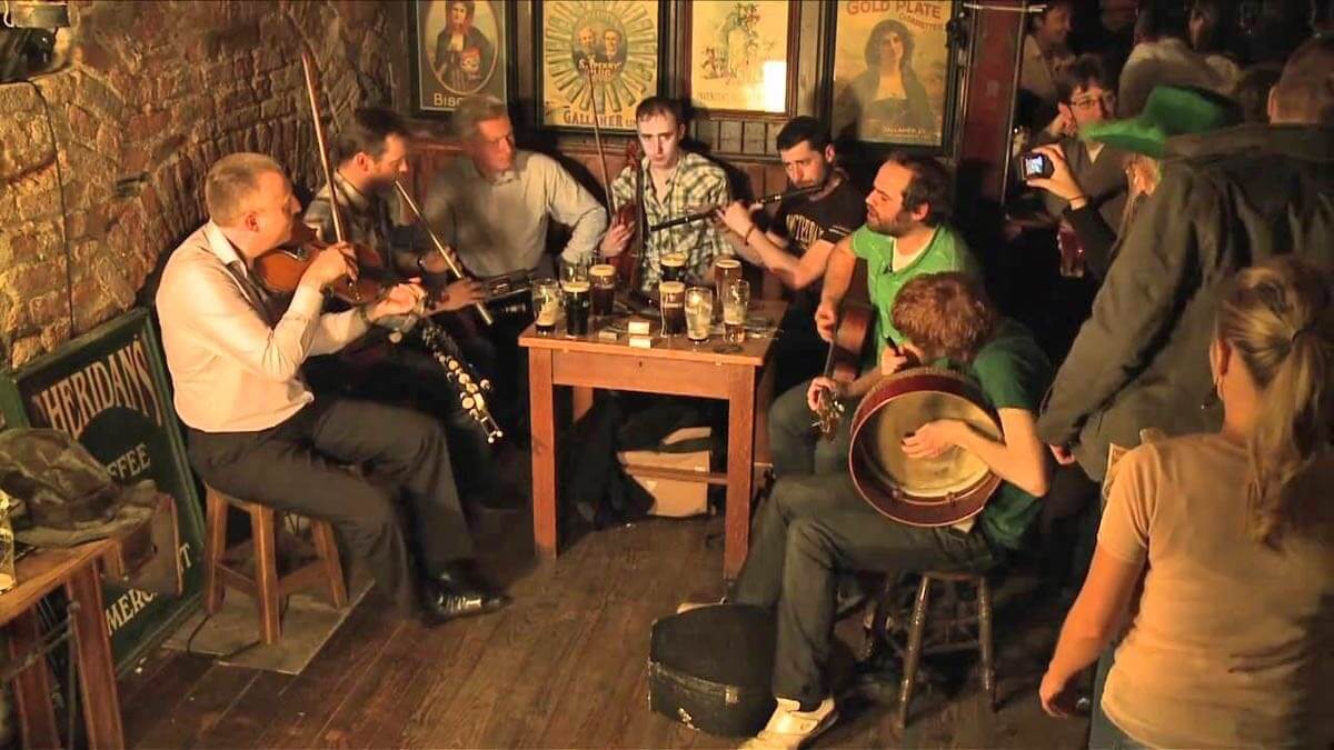 Músicos tocando en un pub tradicional en Irlanda, con violín, guitarra y bodhrán.