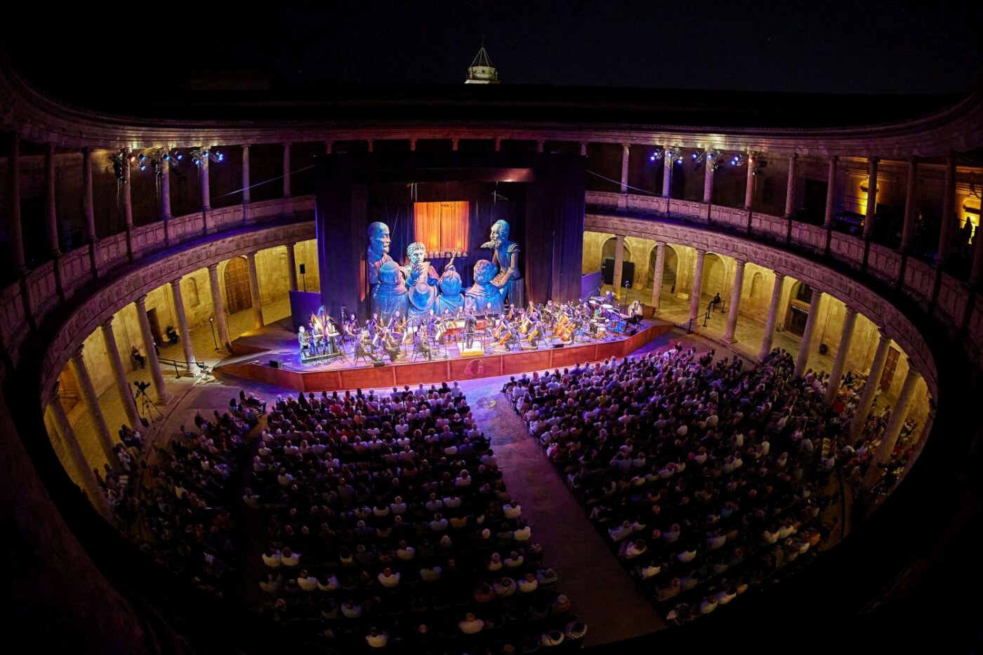 Concierto sinfónico en el Palacio de Carlos V, con una orquesta interpretando bajo el cielo nocturno de Granada.