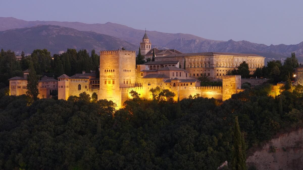 Vista panorámica de la Alhambra iluminada al atardecer, con la imponente Sierra Nevada de fondo.  