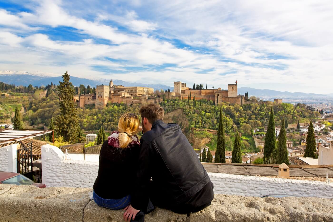 Pareja disfrutando de una vista privilegiada de la Alhambra desde el Mirador de San Nicolás, con el paisaje urbano de Granada.  