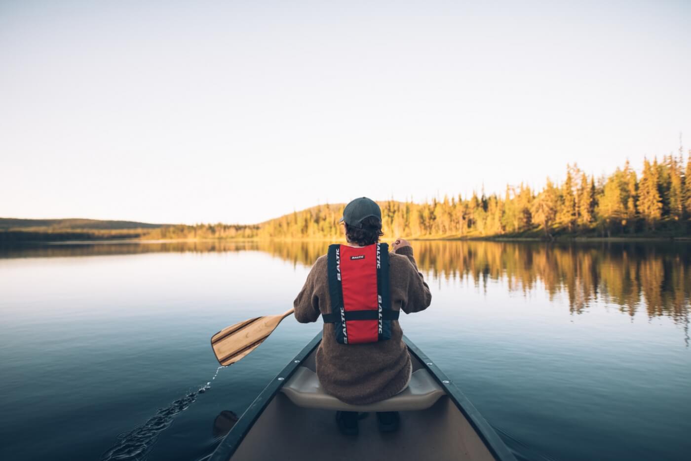 Persona remando en kayak sobre las aguas tranquilas del lago Inari al atardecer, en Laponia.